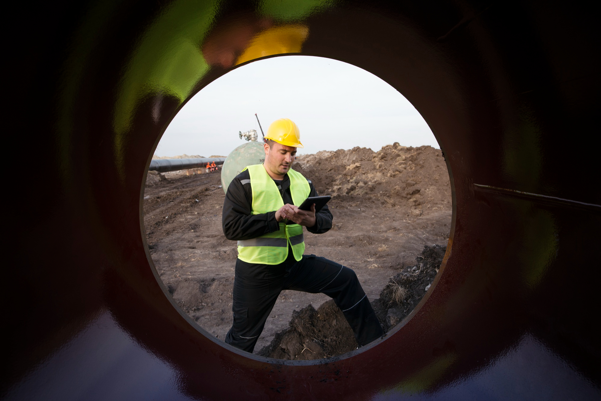 A worker with a safety hat, standing in front of a confined space entrance.